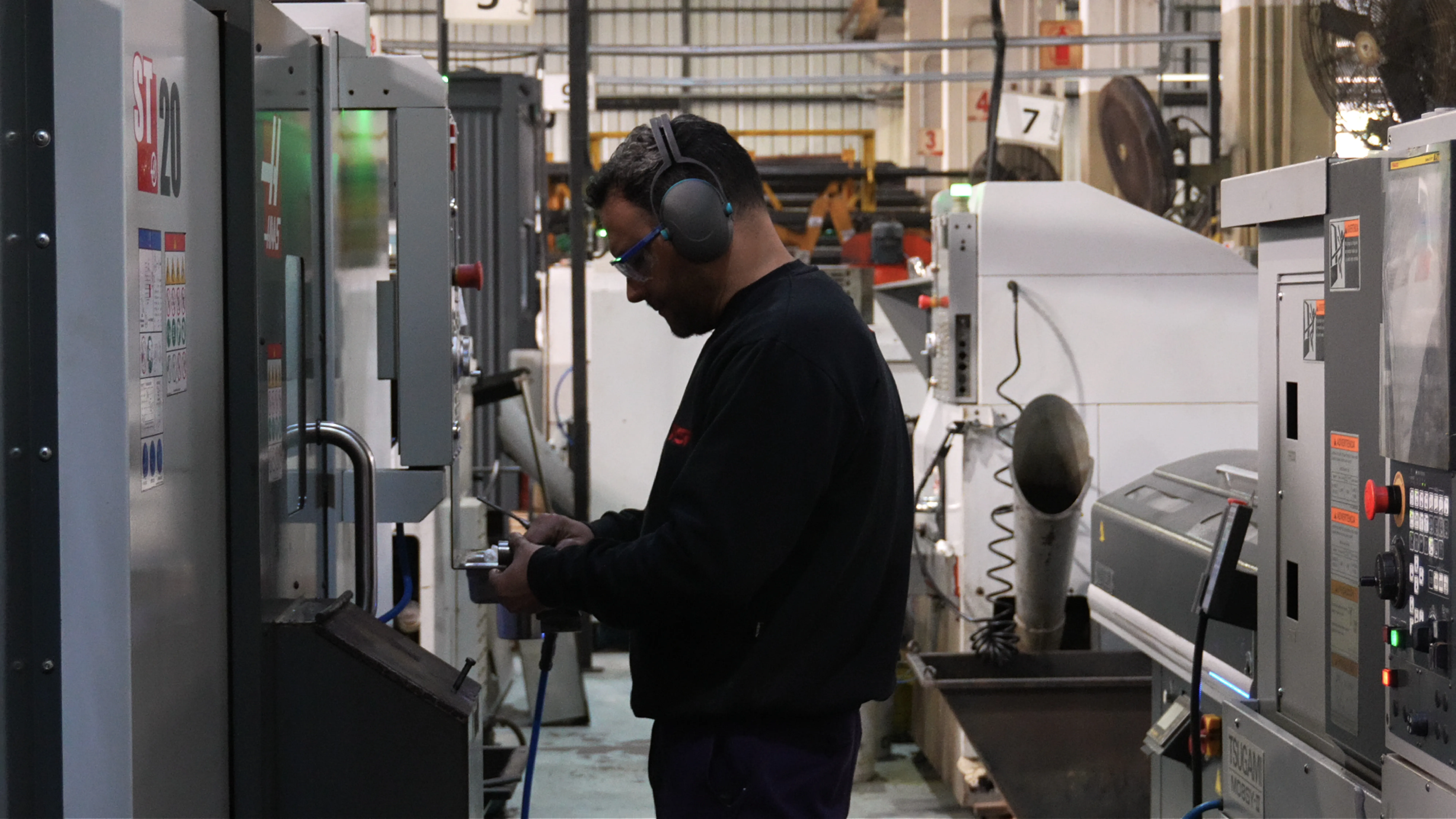 Operario de HSF con protectores auditivos controlando una pieza junto a un torno CNC